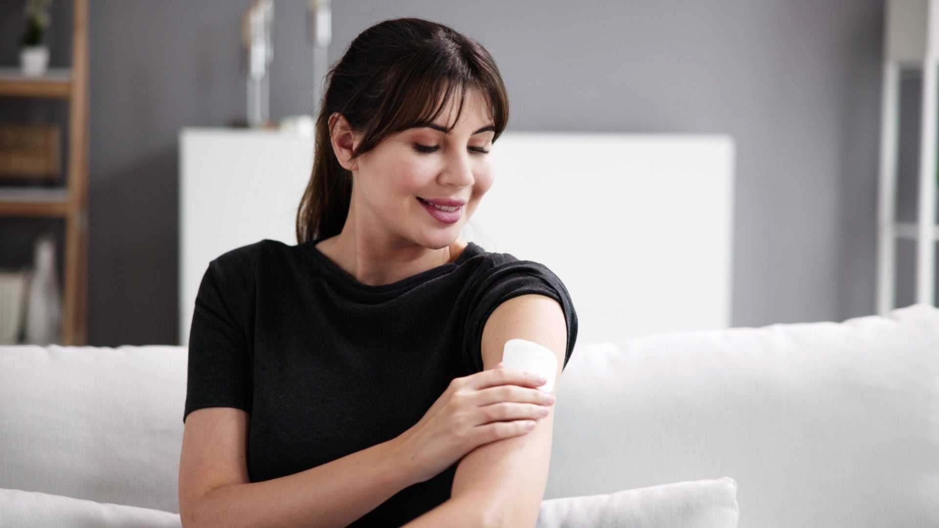 Woman applying a menopausal hormone therapy patch on her arm while sitting on a couch