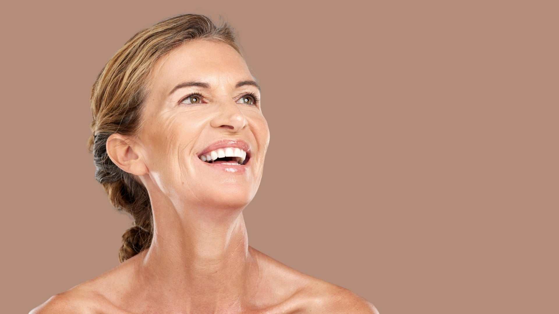 Middle-aged woman smiling with uplifted mouth corners against a plain background representing Smile Lift Botox benefits