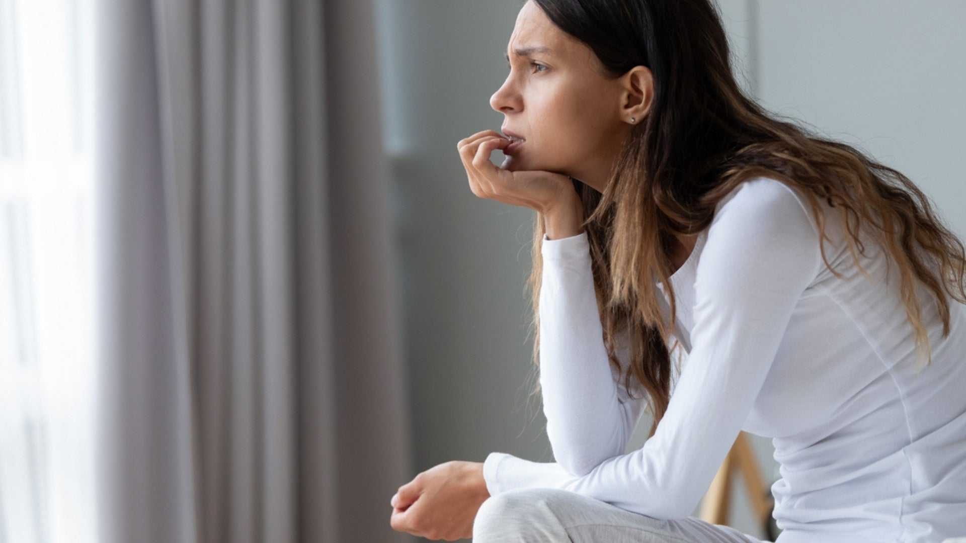 Stressed woman with long hair in white shirt looking worried, illustrating how stress affects skin and benefits of relaxation