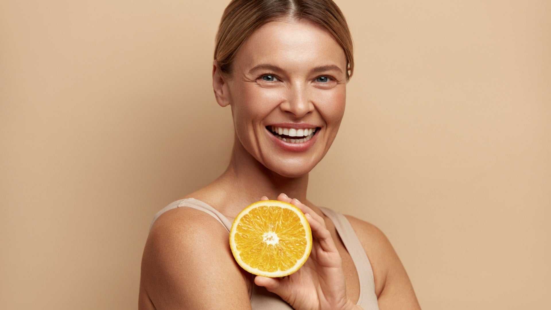 smiling woman holding half an orange representing diet for healthy glowing skin