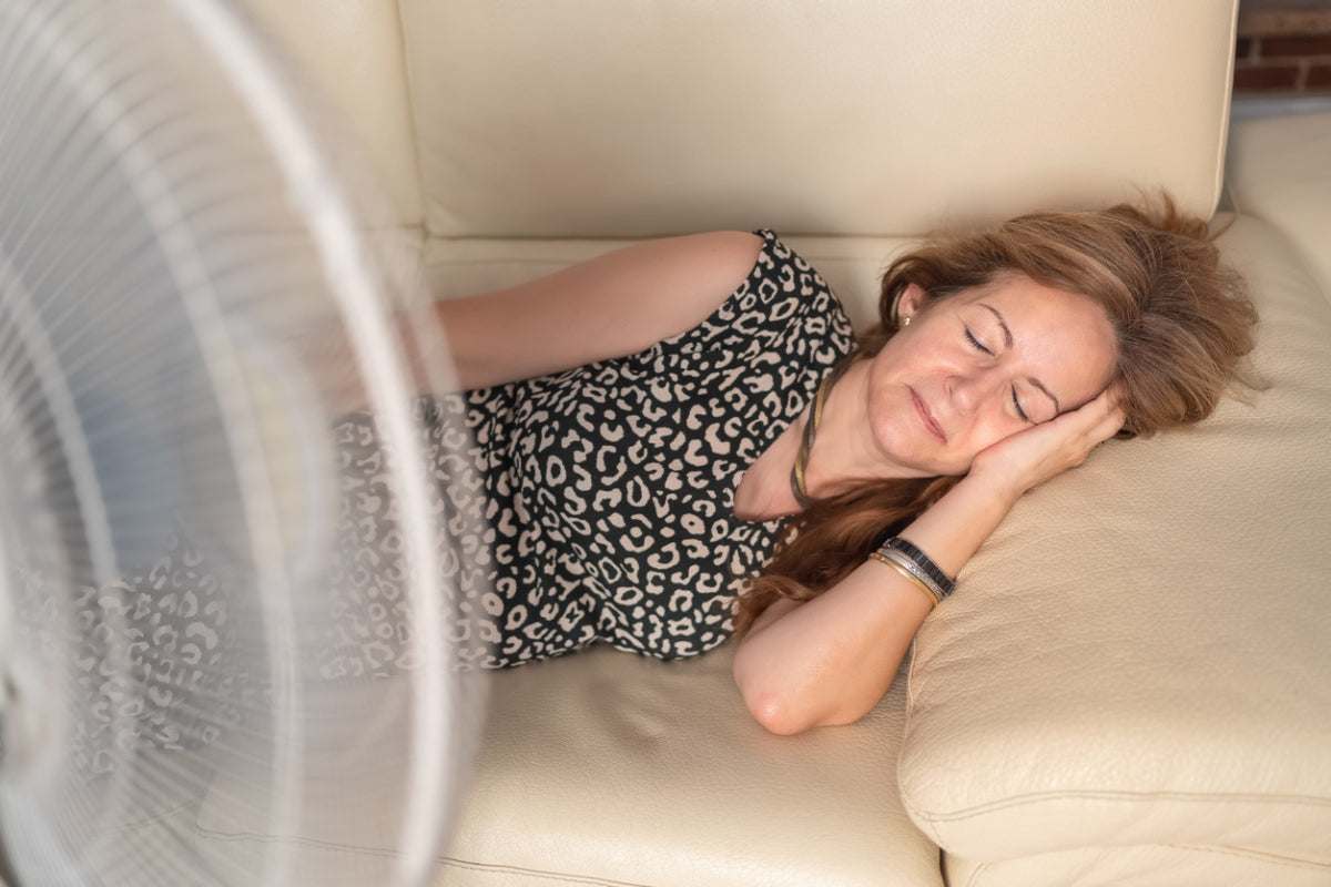 Middle-aged woman resting on a couch with a fan blowing, symbolizing relief from hot flashes during menopause.