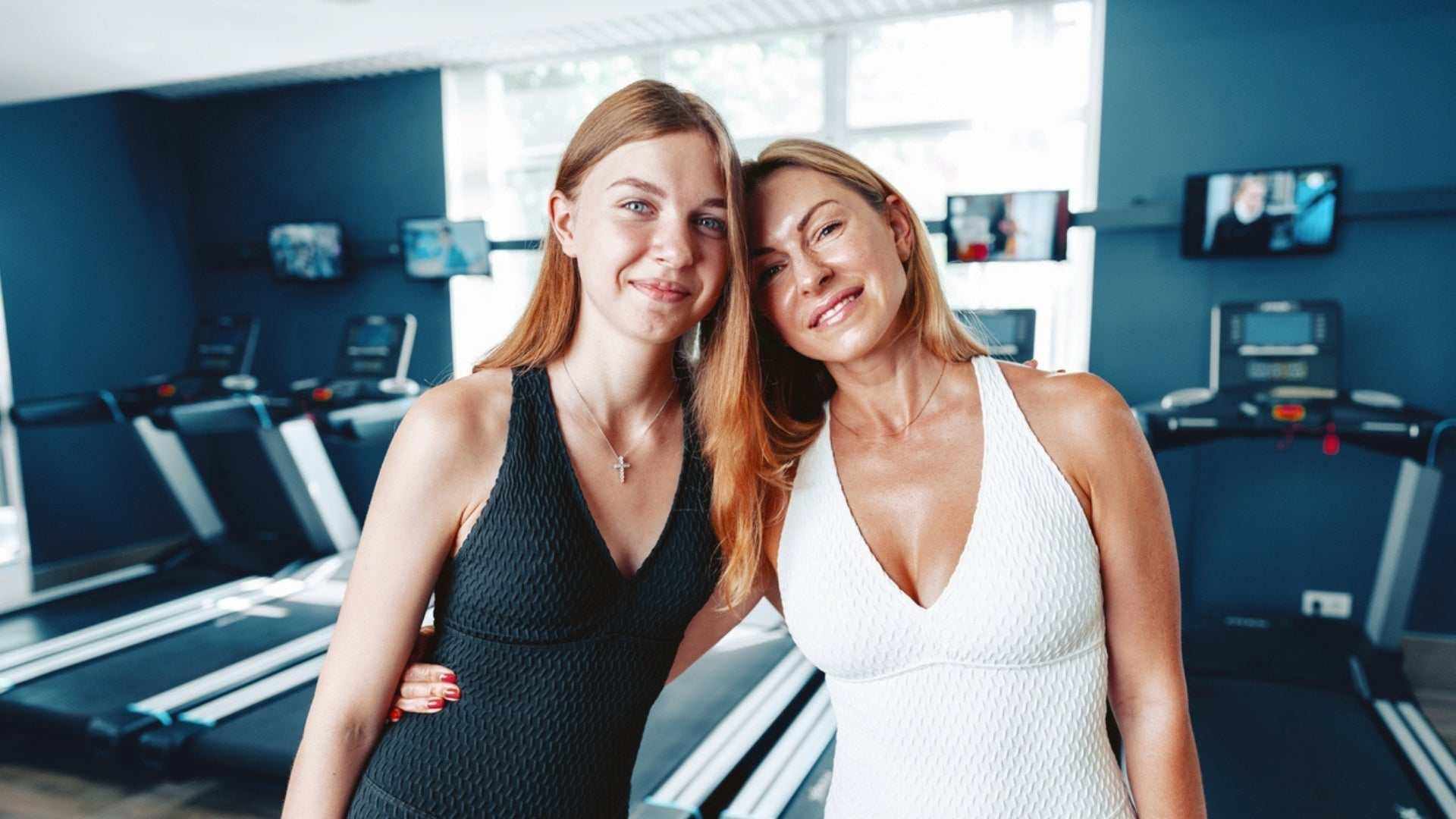 two women in workout attire posing in a gym with treadmills in the background exercise after botox guidance concept