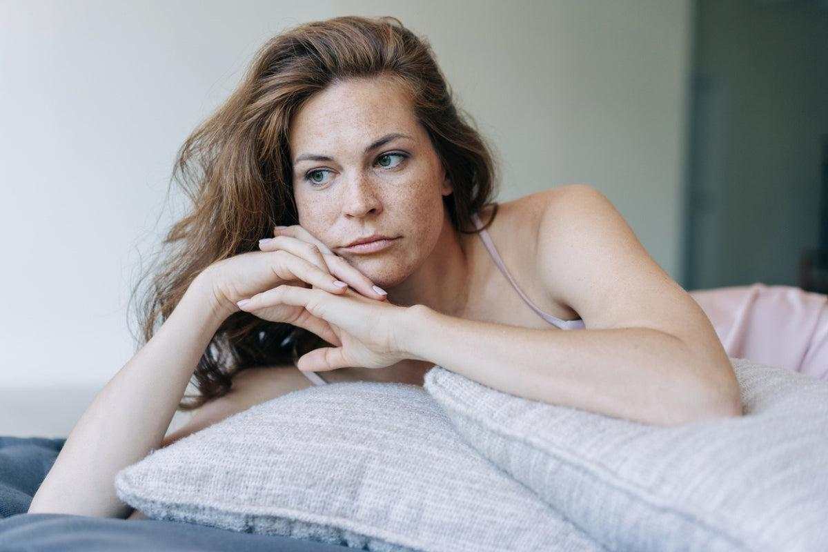 Middle-aged woman looking contemplative, illustrating genitourinary syndrome of menopause and related emotional impact.