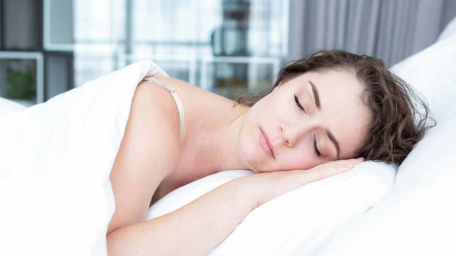 Woman peacefully sleeping on white bed highlighting sleep and skin health benefits