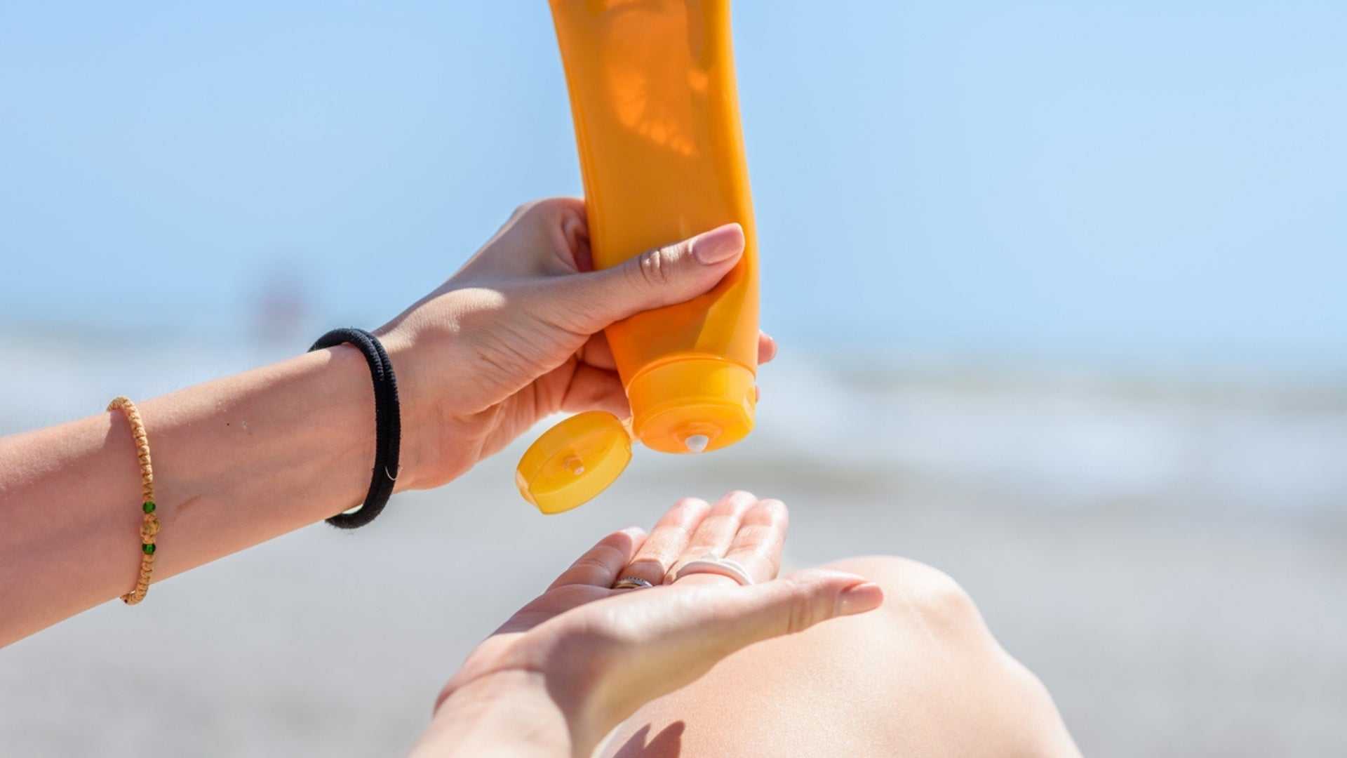 Person applying sunscreen lotion on hand at the beach for sun protection