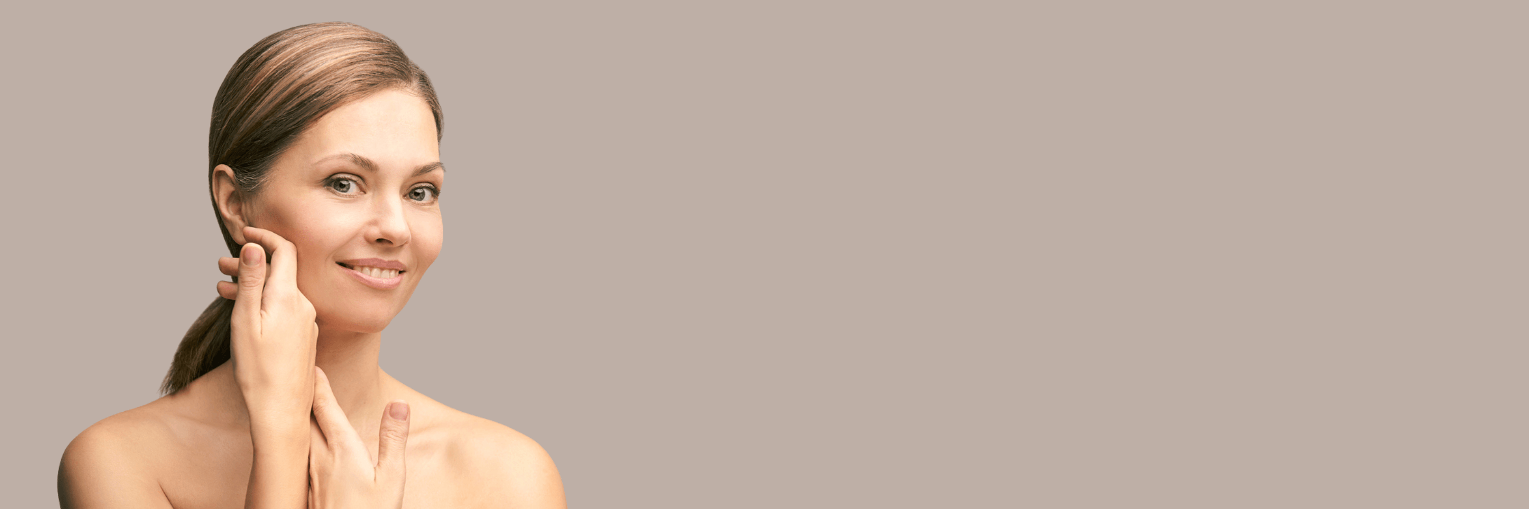 Woman applying cream to her face on a beige background