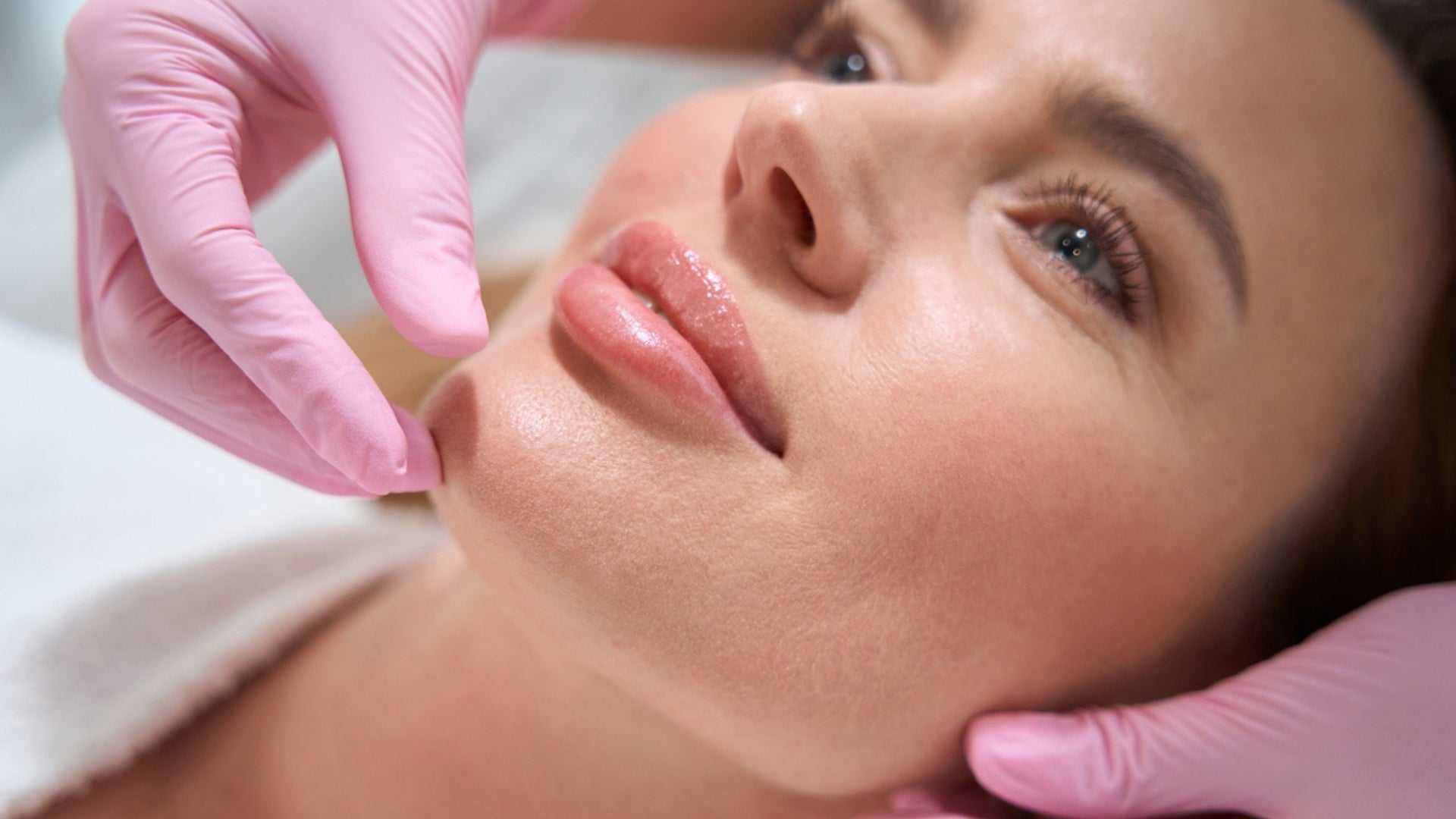 Close-up of a woman receiving a lip injection procedure by a practitioner wearing pink gloves.