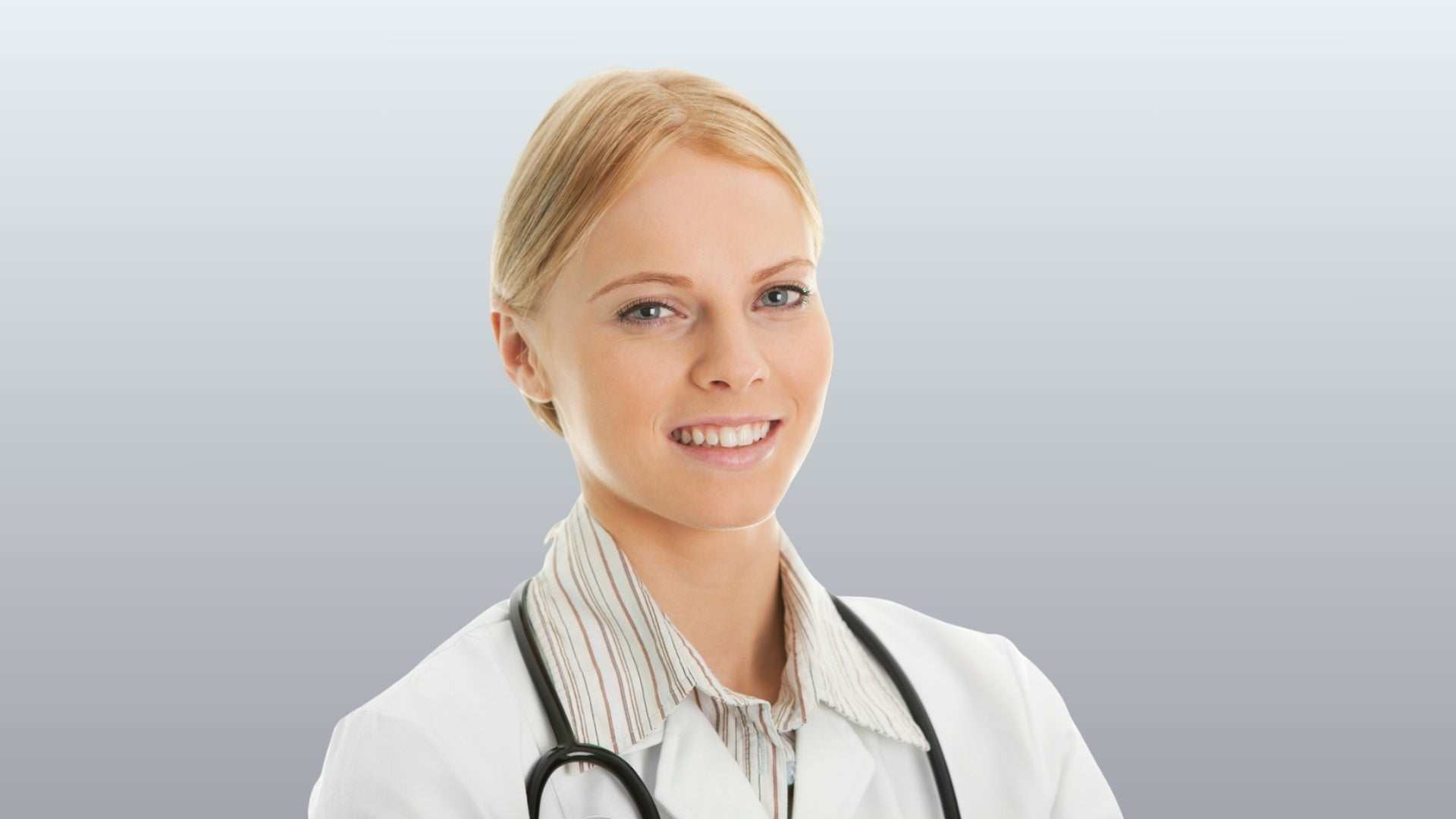 Smiling female dermatologist in a white coat with stethoscope against grey background, representing best dermatologist in Oakville.