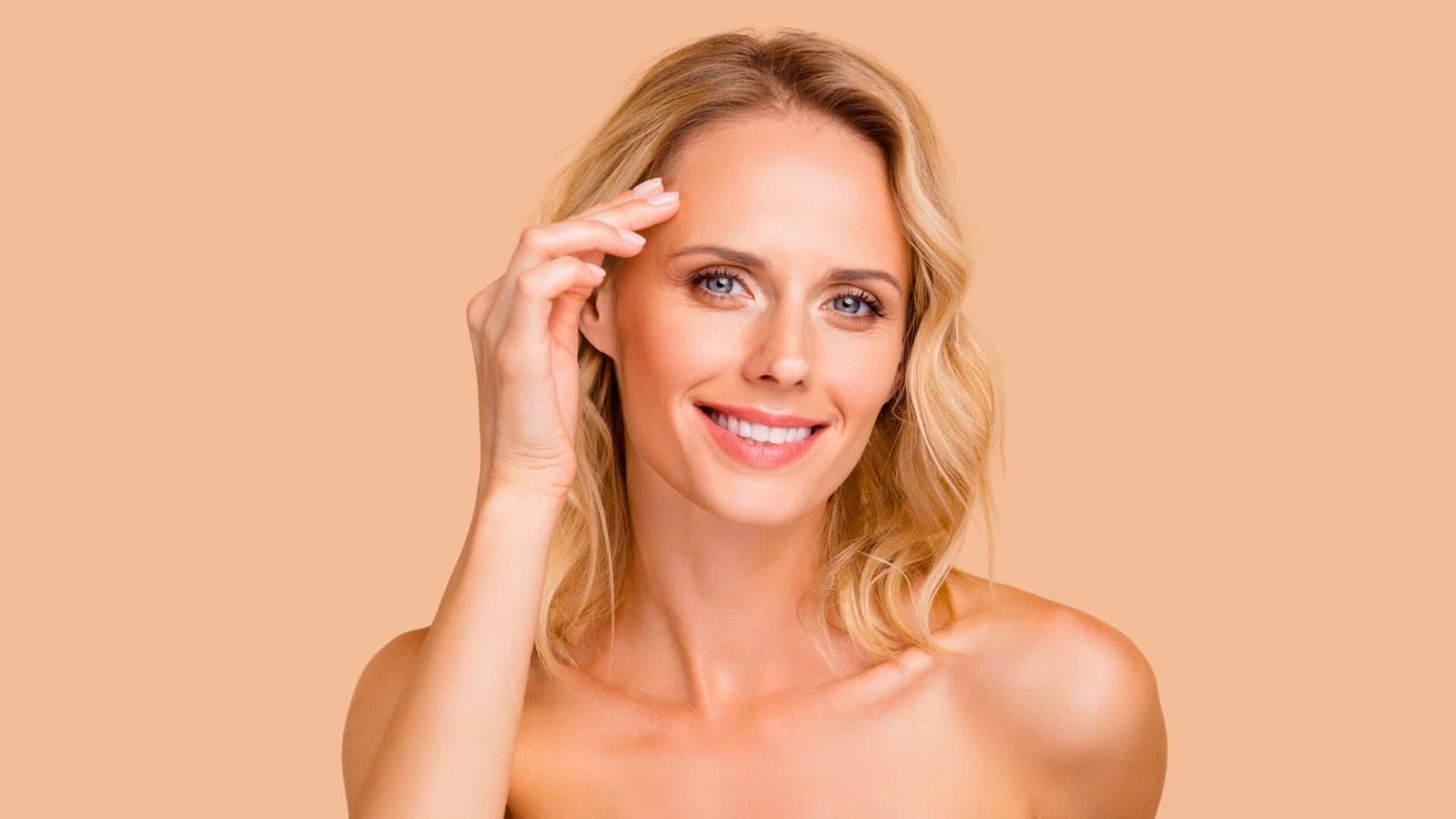 Smiling blonde woman touching forehead demonstrating smooth skin after Botox for forehead treatment