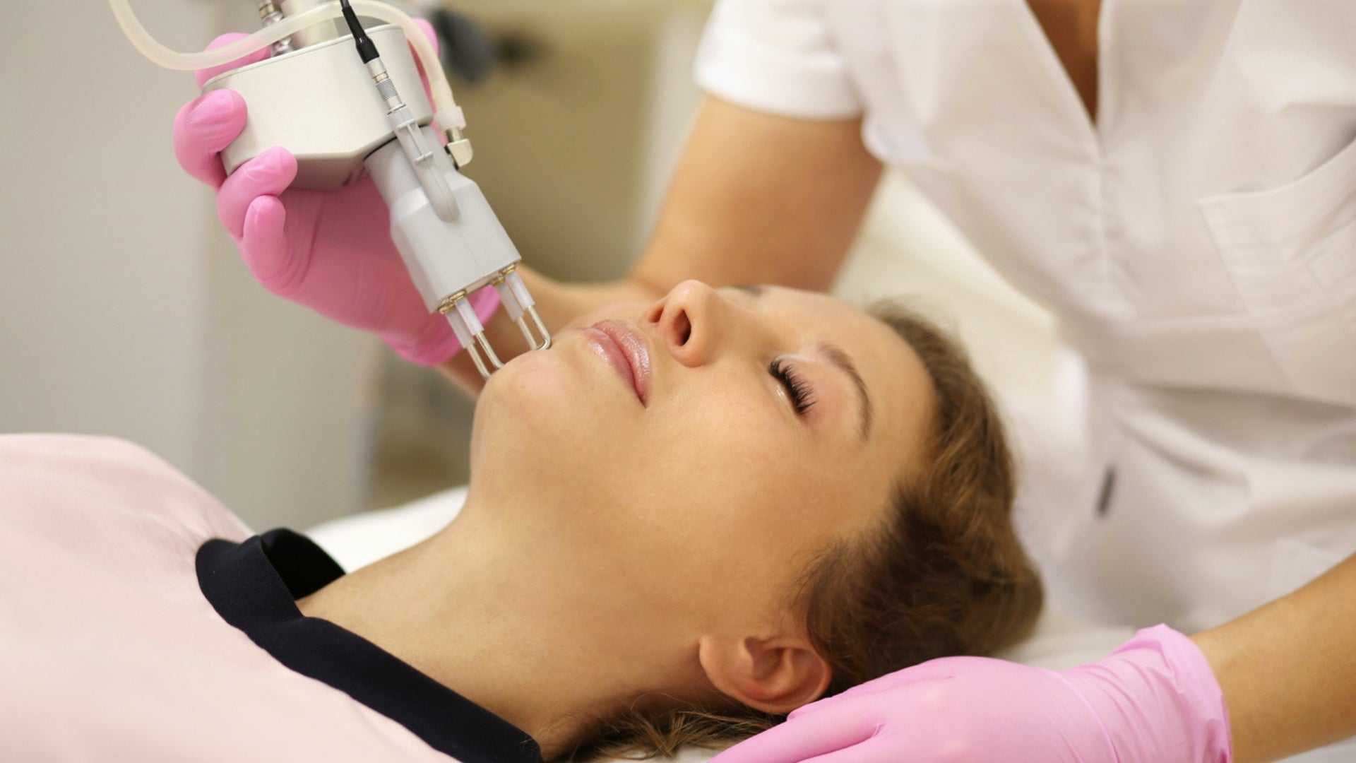 Woman receiving CO2 laser skin treatment on face by professional in clinic, illustrating cost of CO2 laser treatment options.