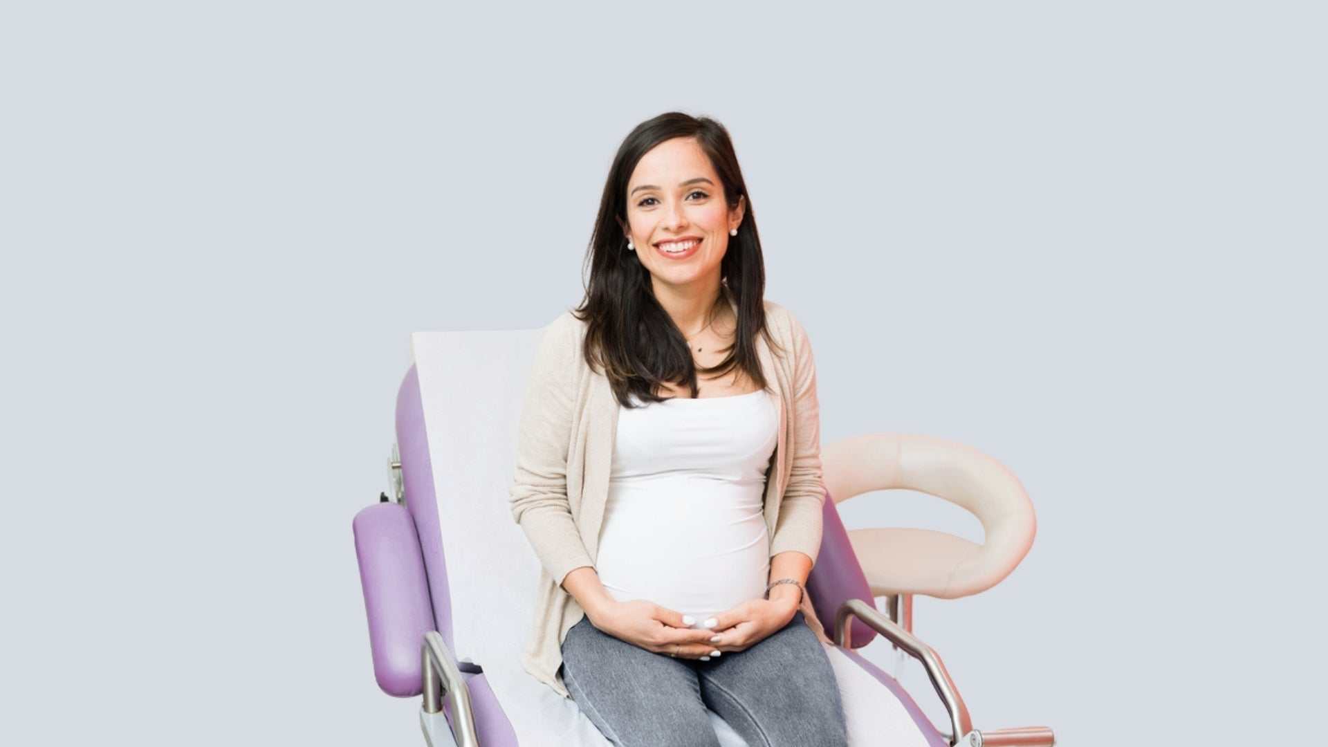 Pregnant woman smiling while seated on a purple medical chair, holding her belly, representing questions about getting botox during pregnancy.