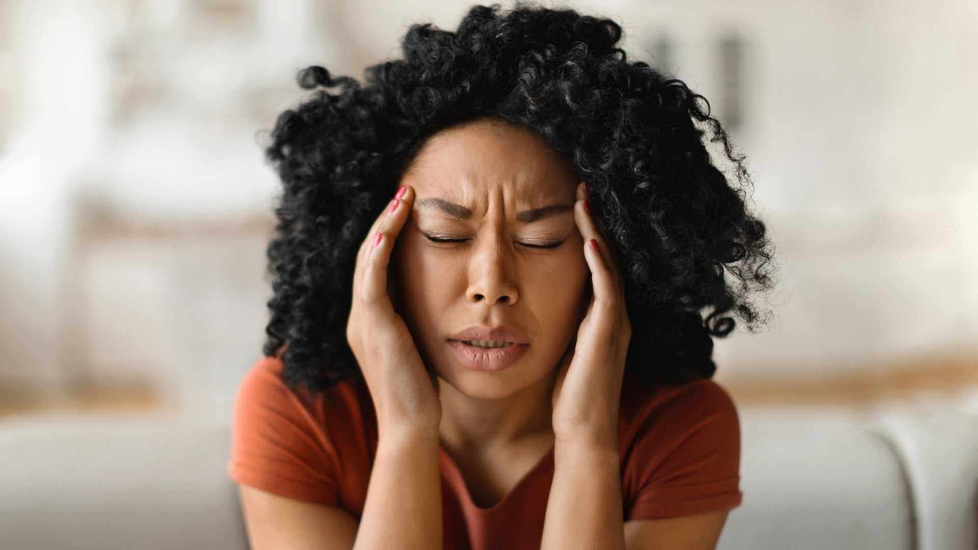 Woman with curly hair pressing temples in pain, representing migraine discomfort and botox treatment cost consideration.