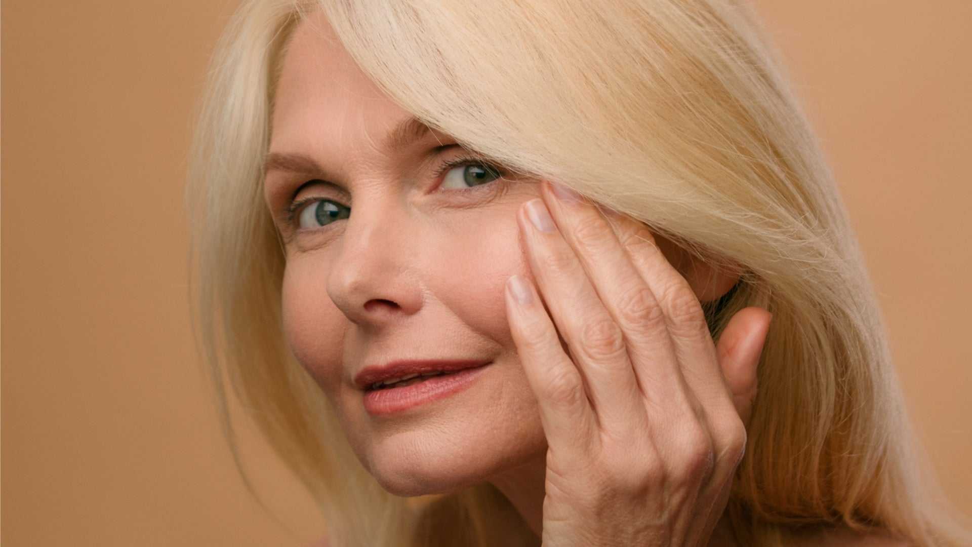 Mature woman with smooth skin gently touching her face representing biostimulation therapies for collagen and elastin regeneration.