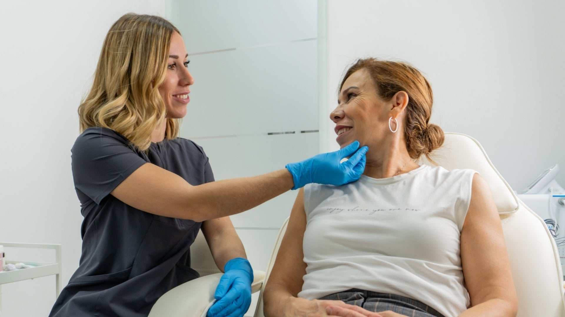 Clinician wearing blue gloves consulting and examining patient's jaw for masseter botox treatment in a modern clinic setting