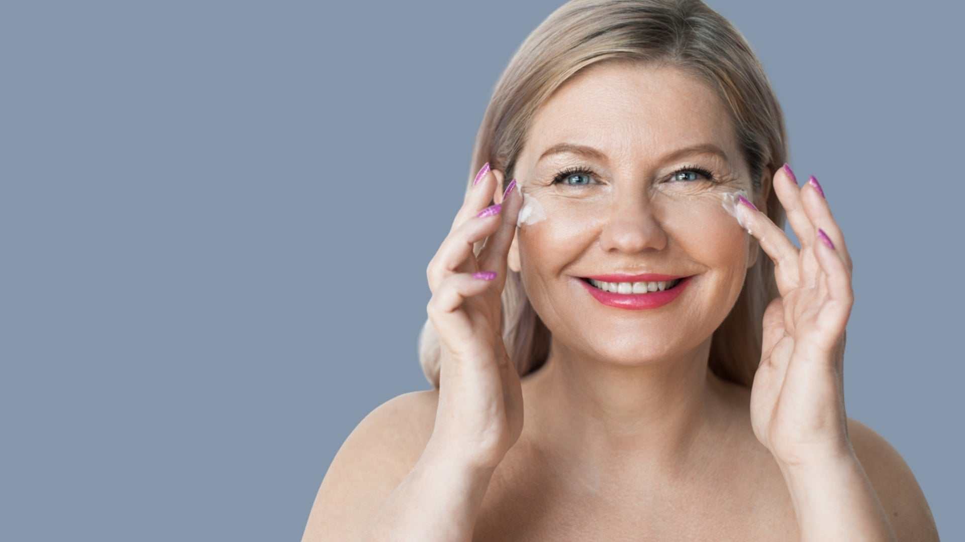 Smiling woman applying moisturizer with SPF to her face against a blue background