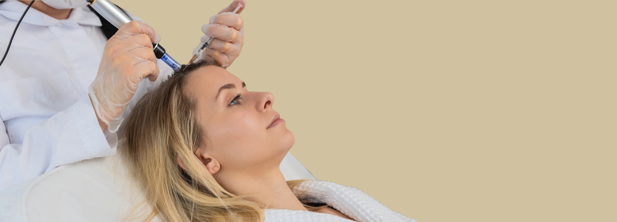 A woman lies on a treatment chair while a practitioner in a white coat uses a handheld cosmetic device on her forehead, against a plain beige background.