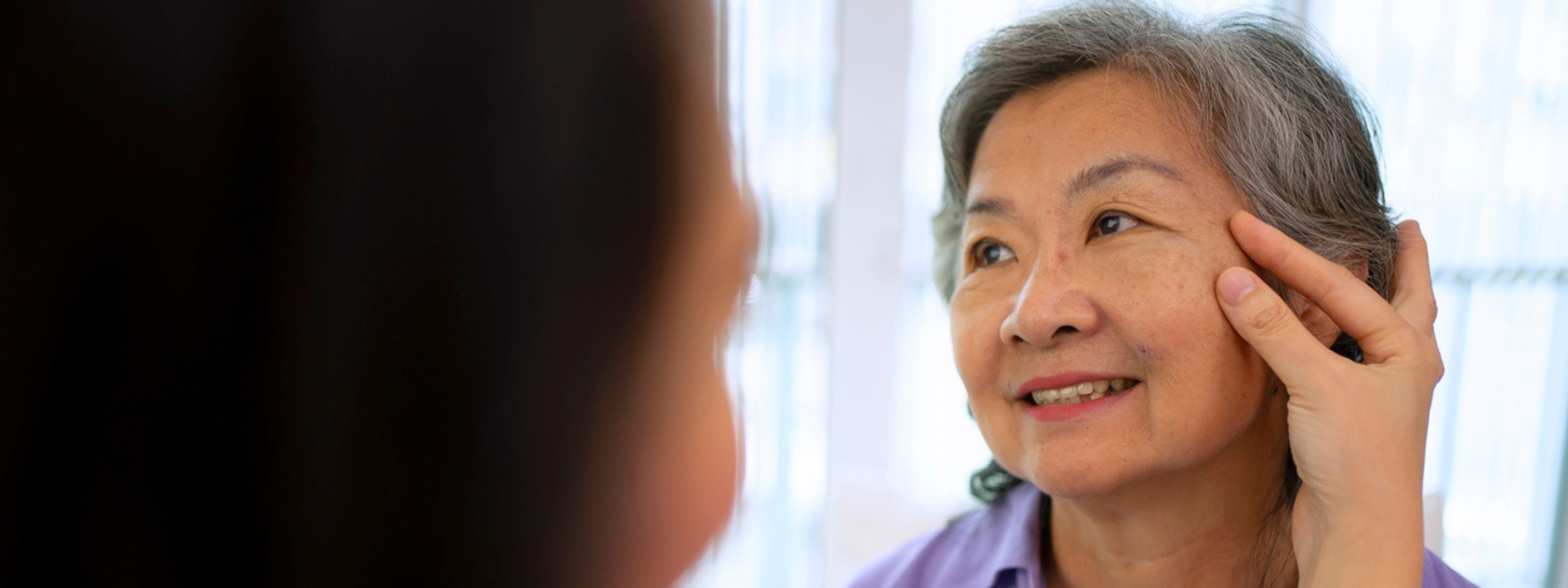 Woman examining her face in a mirror, possibly checking for signs of aging.