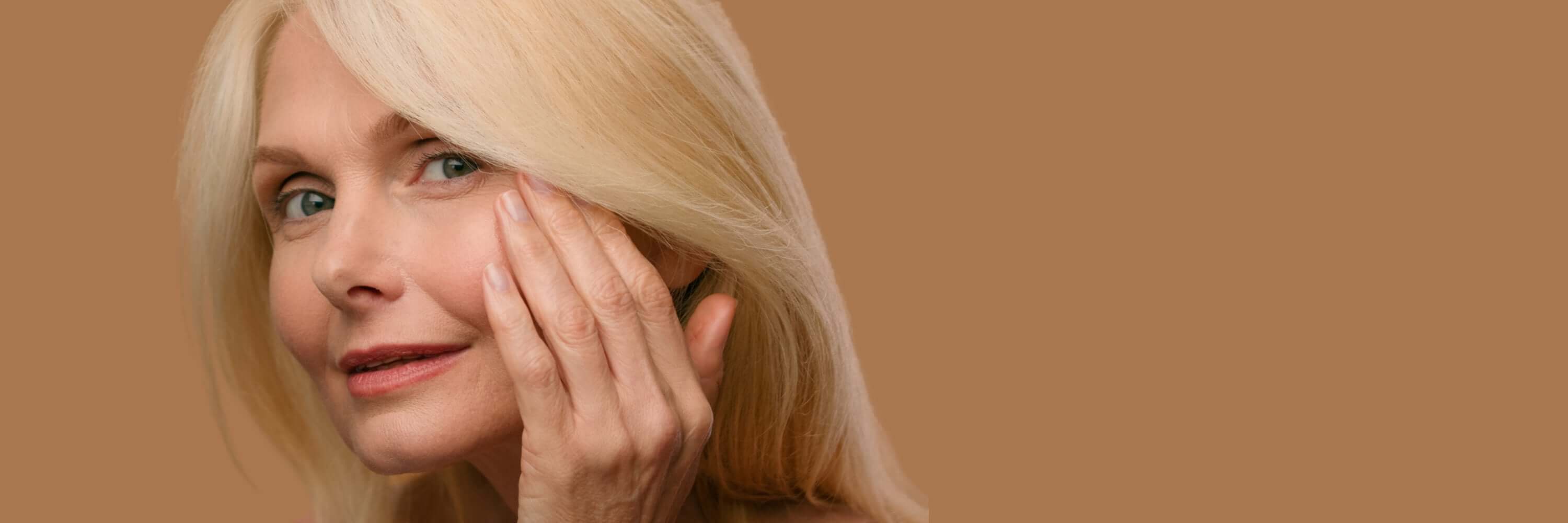 Woman with blonde hair touching her face against a beige background